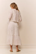 Woman wearing a white lace eyelet maxi skirt and matching long sleeve blouse against a plain background