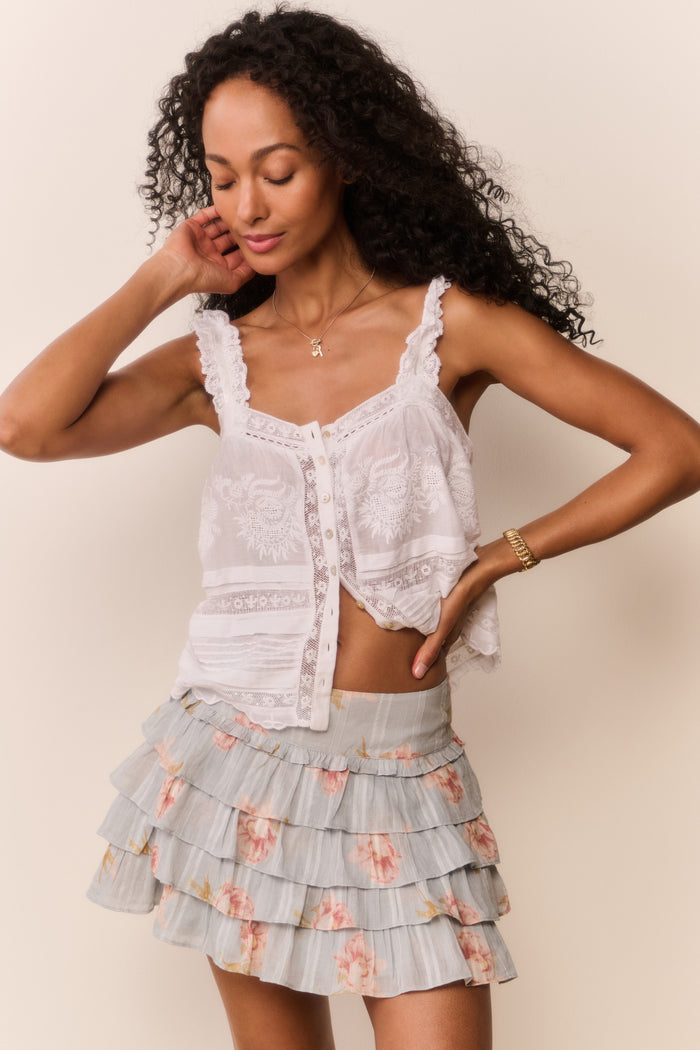 Woman wearing a white lace top and floral tiered skirt against a beige background