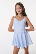 Young girl wearing a light blue dress with thin straps on a white background