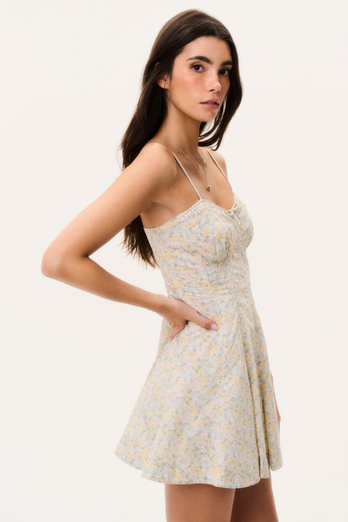 Woman wearing a floral mini dress with thin straps on a plain background