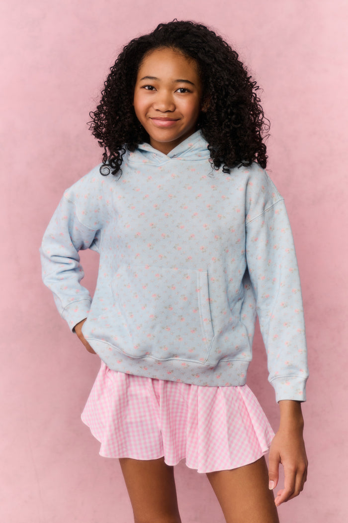 Girl wearing a light blue hoodie and pink gingham skirt on a pink background