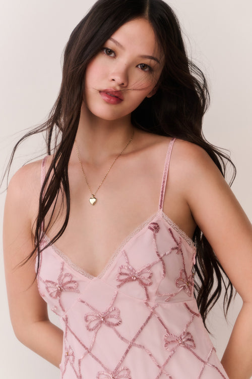 Woman wearing a pink lace mini dress with bow pattern embellishments on a white background