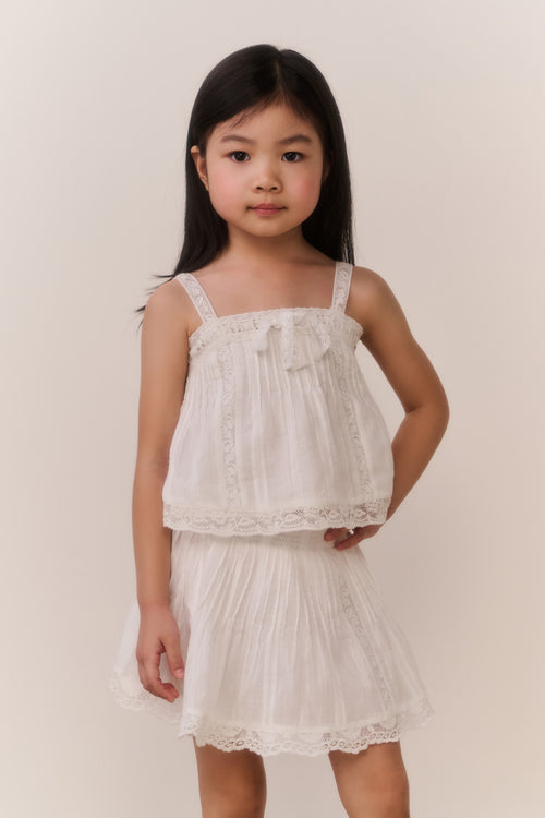 Little girl wearing a white lace camisole and matching skirt against a plain background