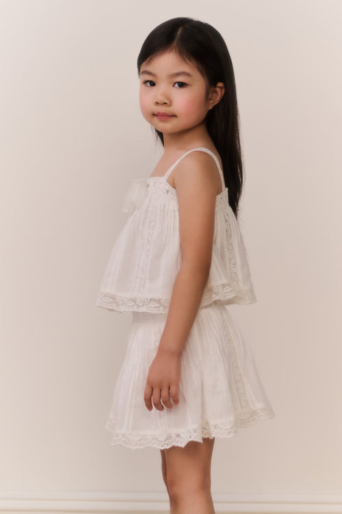 Little girl wearing a white lace camisole and matching skirt against a plain background