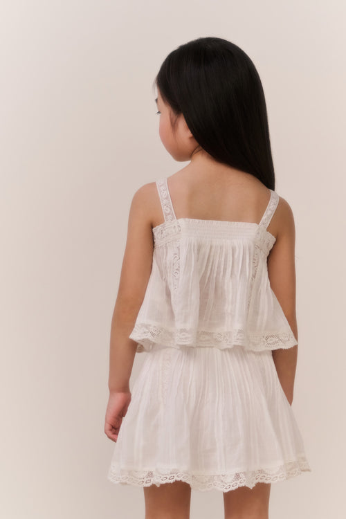 Little girl wearing a white lace camisole and matching skirt against a plain background