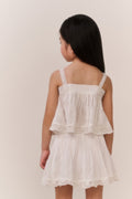 Little girl wearing a white lace trim camisole and matching skirt against a plain background
