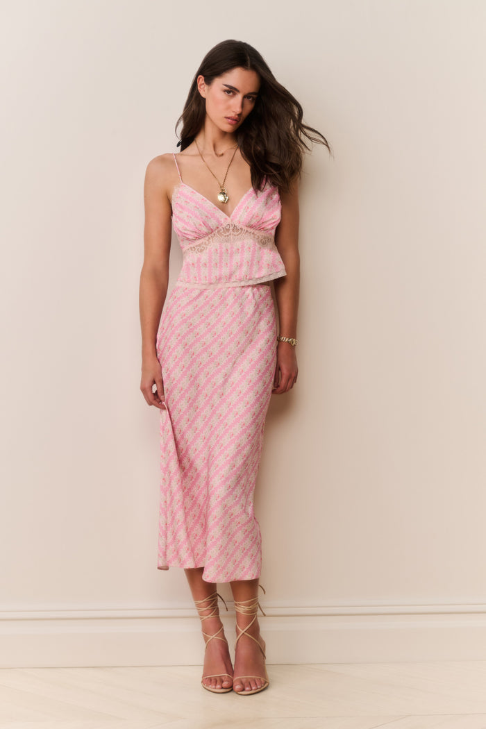 Woman wearing a pink patterned matching skirt and camisole with a white background