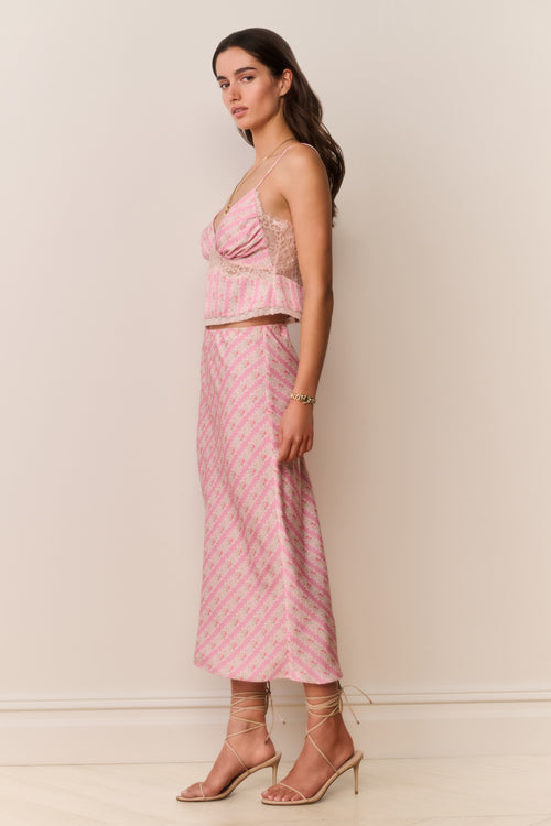 Woman wearing a pink patterned matching skirt and camisole with a white background