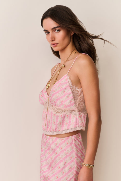 Woman wearing a pink striped camisole and matching skirt with lace details on a beige background
