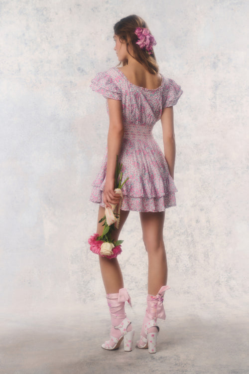 Woman in a pink dress with puffed sleeves and matching shoes holding flowers against a light background