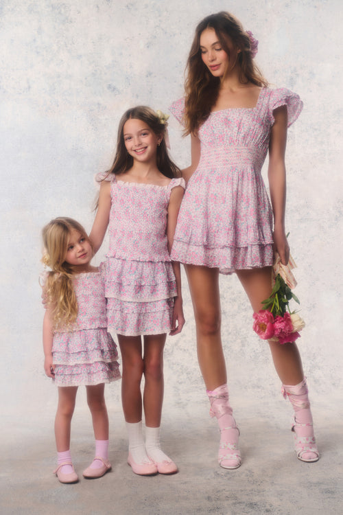 Two girls and a young woman wearing matching pink dresses against a light background