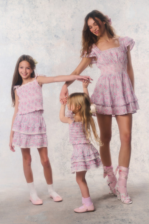 Three women in matching pink outfits standing together against a light background