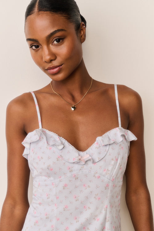 Woman wearing a blue floral ruffle hem mini dress with thin straps against a beige background