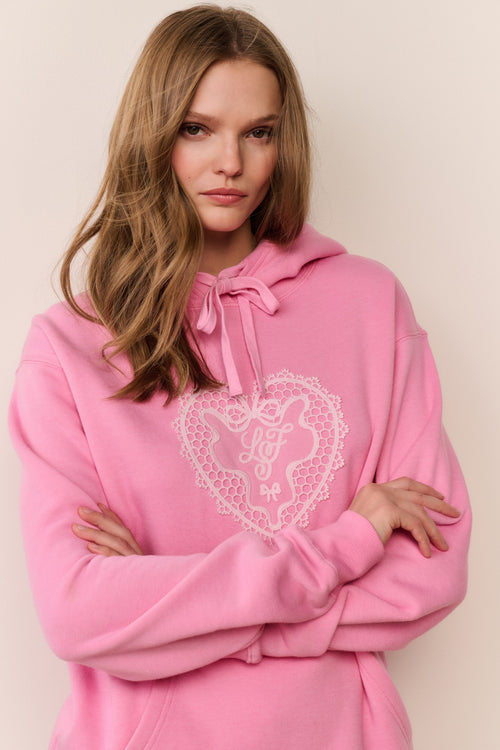 Person wearing a pink hoodie with a heart design on a plain background