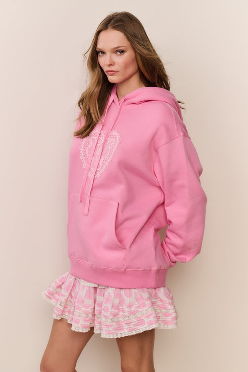 Woman wearing a pink hoodie and patterned skirt against a beige background