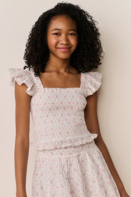 Young girl wearing a white floral ruffle top and matching skirt against a plain background