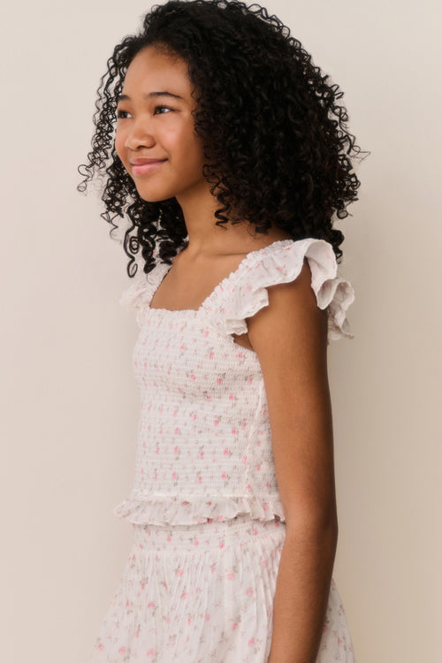 Young girl wearing a white floral ruffle top and matching skirt against a plain background