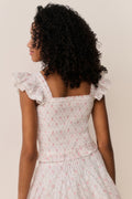 Girl wearing a white floral Ruffle top with matching skirt against a beige background