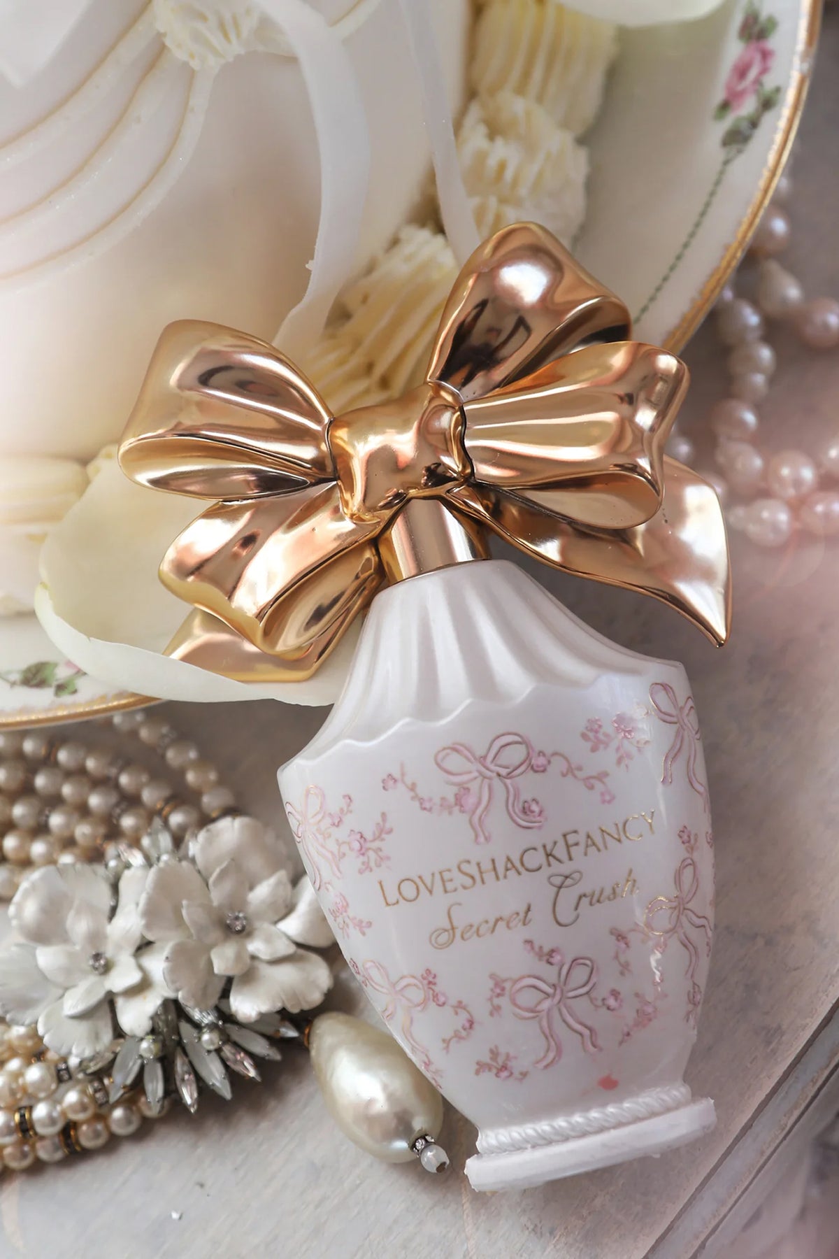 White LoveShackFancy heart perfume bottle with gold bow, pearls and floral decor.
