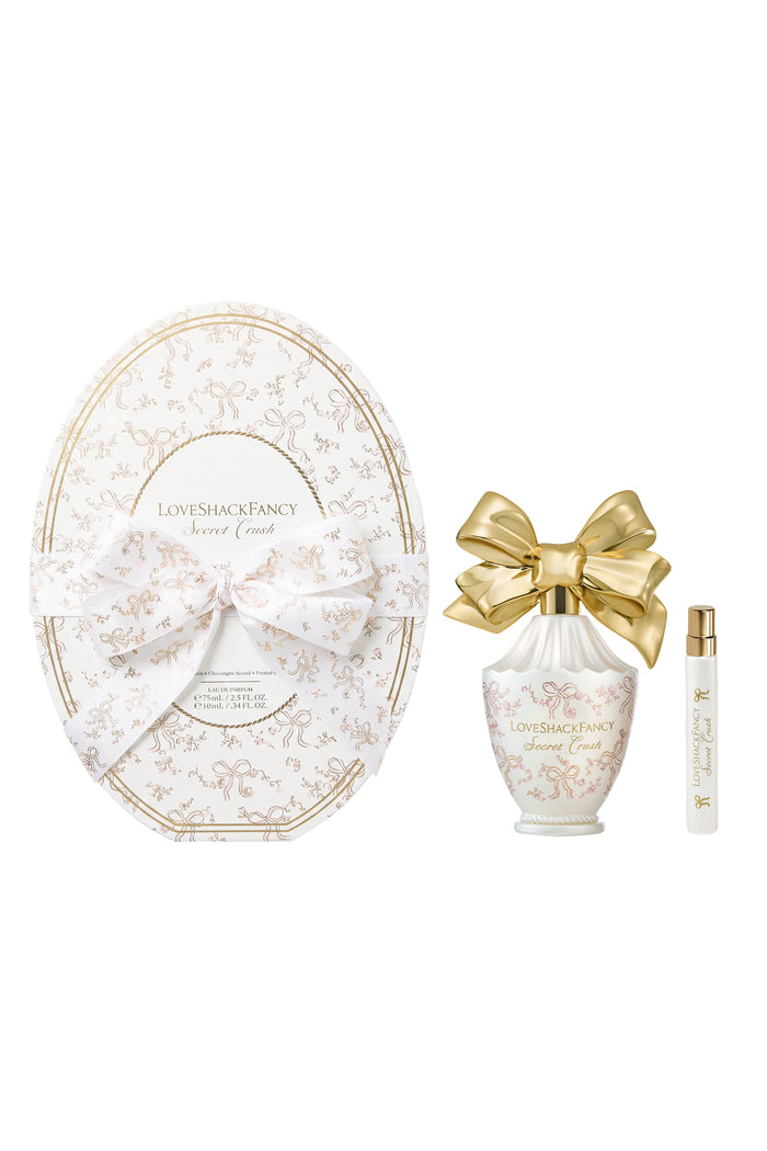 Oval LoveShackFancy gift packaging with white heart bottle and gold bow plus travel spray.
