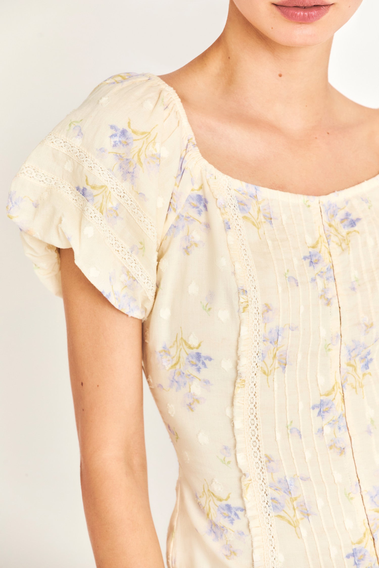 The Zia top is a Victorian-inspired soft yellow fitted corset top that features a stunning textured clip dotted heart shape dobby fabric that gives it an antique feel. It features delicate custom lace detail and an elasticated shoulder to wear off or on the shoulder. It also features a baby blue flower print. 