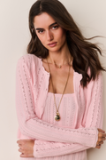 Woman wearing a pink knitted dress and cardigan set against a plain background