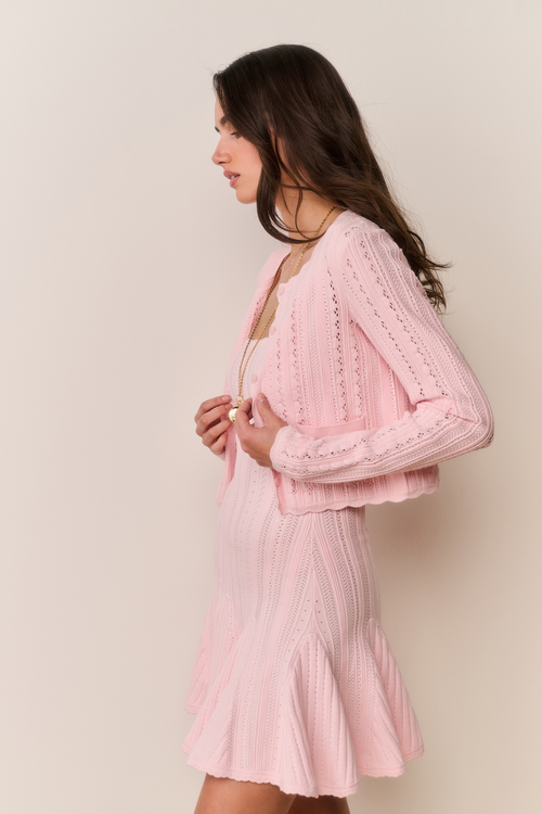 Woman wearing a pink dress and cardigan against a plain background