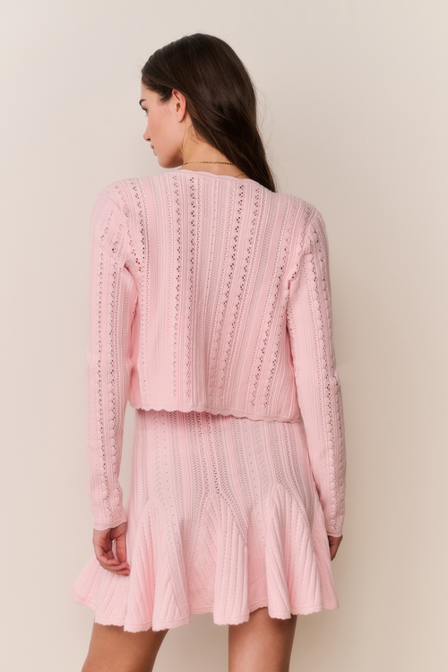 Woman wearing a pink knitted dress and cardigan set against a plain background