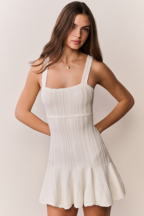 Woman wearing a white knit dress with thin straps on a plain background