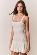 Woman wearing a white knit dress with thin straps on a plain background