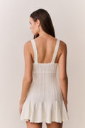 Woman wearing a white knit dress with thin straps on a plain background