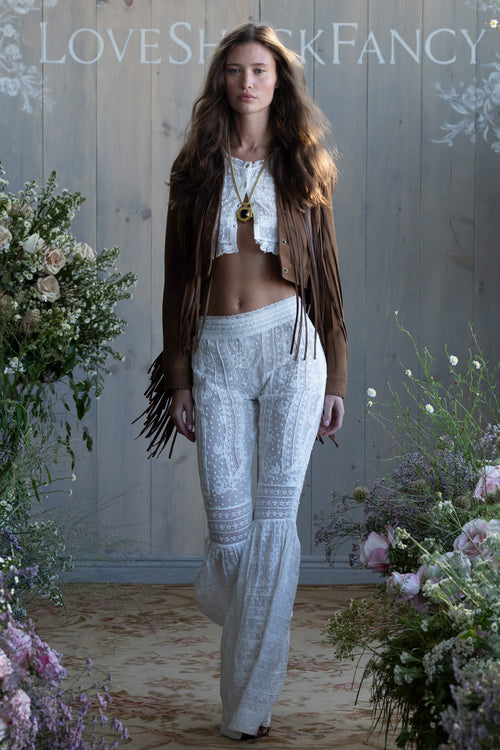 Woman in a white cotton outfit with floral decorations and 'LOVE SHACK FANCY' branding.