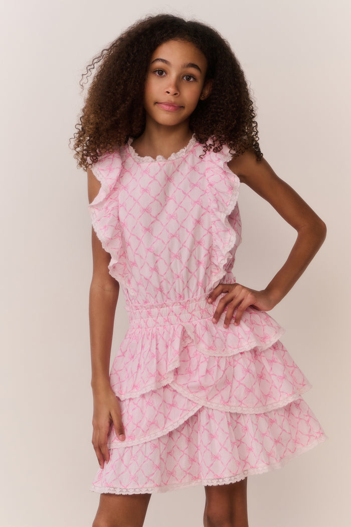 Young girl wearing a pink bow print dress against a plain background