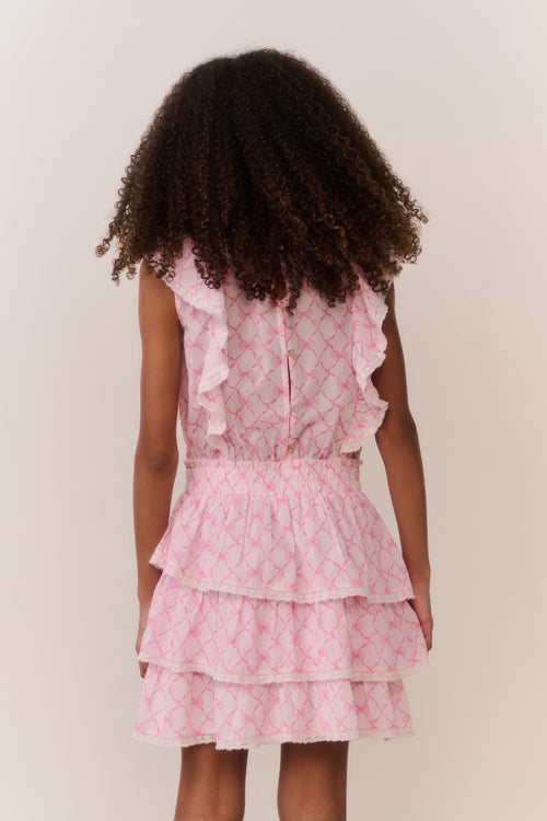 Girl wearing a pink bow print dress with ruffled layers on a plain background