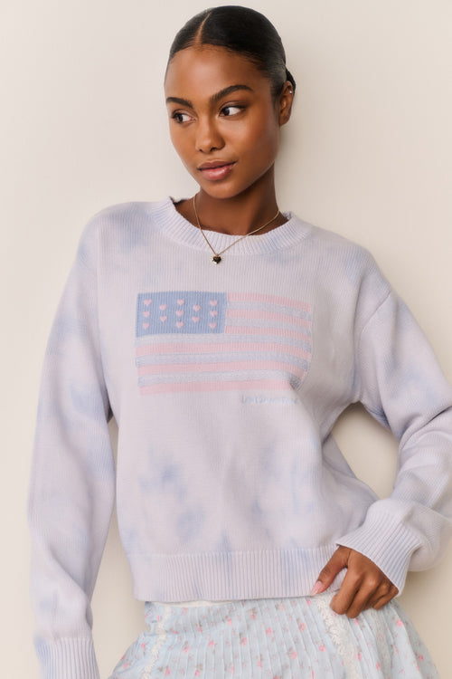 Woman wearing a blue tie-dye sweater with an American flag design against a plain background