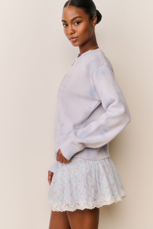 Woman wearing a Light blue tie-dye sweater with American flag design and a floral skirt against a beige background