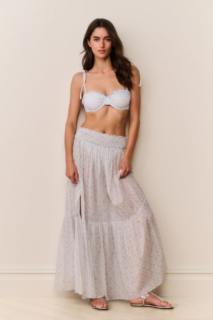 Woman wearing a blue floral bikini top and light gray skirt against a plain background