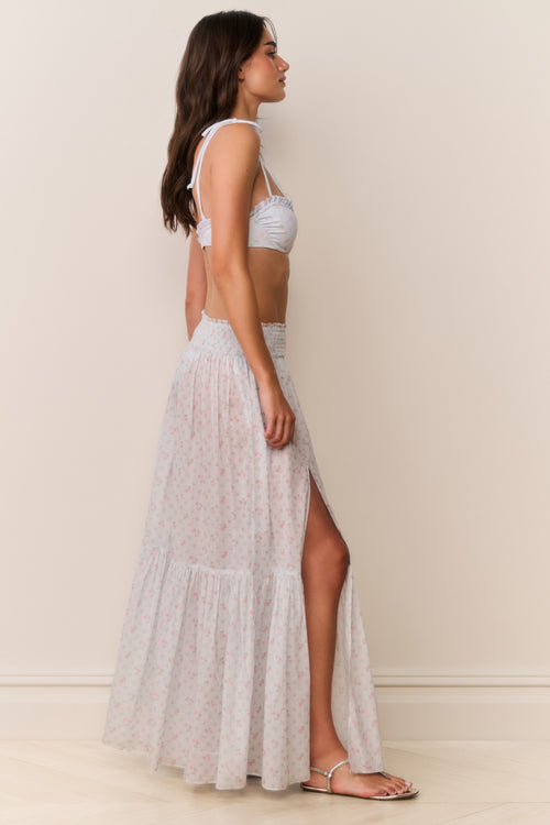 Woman wearing a blue floral bikini top and light gray skirt against a plain background