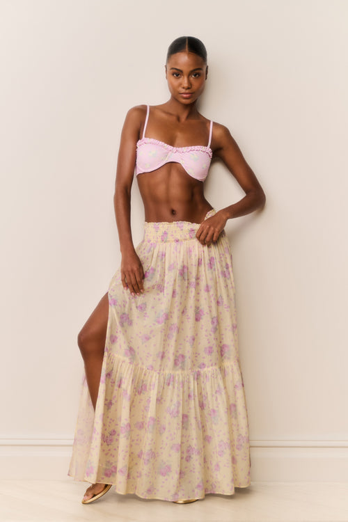 Woman wearing a pink bikini top and floral skirt against a plain background