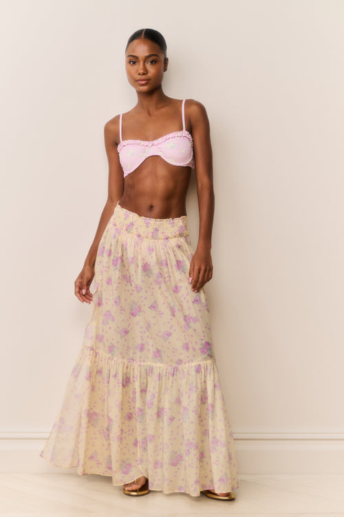 Woman wearing a pink bikini top and floral skirt against a plain background