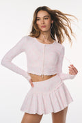 Woman wearing a light pink outfit with a skirt and cropped top on a white background