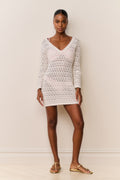 Woman wearing a white crochet dress against a plain background