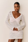Woman wearing a white crochet dress against a plain background