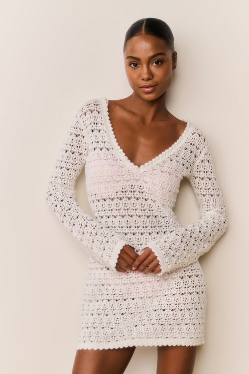Woman wearing a white crochet dress against a plain background