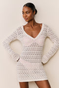 Woman wearing a white crochet dress against a plain background