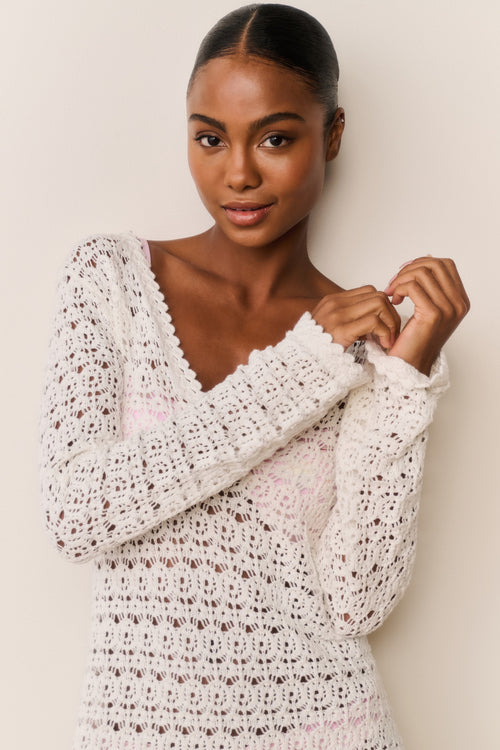 Woman wearing a white crochet dress against a plain background