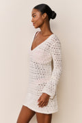 Woman wearing a white crochet dress against a beige background