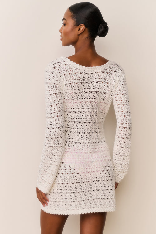 Woman wearing a white crochet dress against a beige background