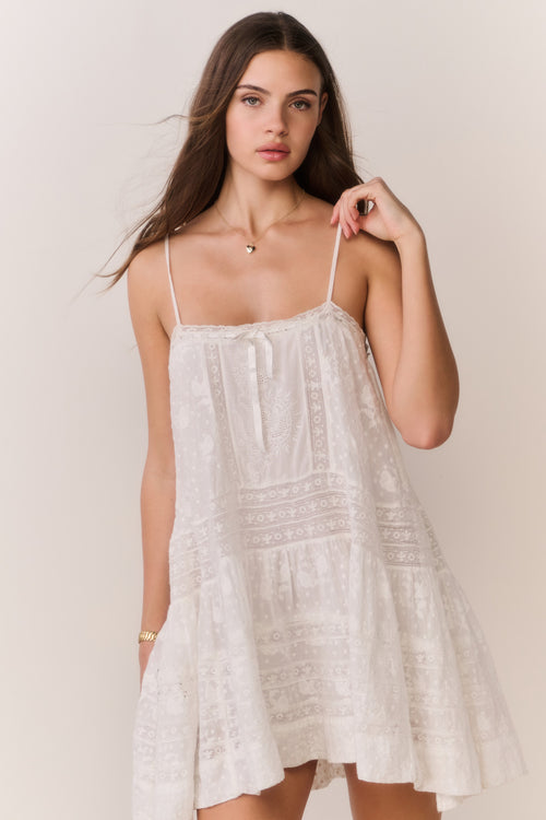 Woman wearing a white lace mini dress against a plain background