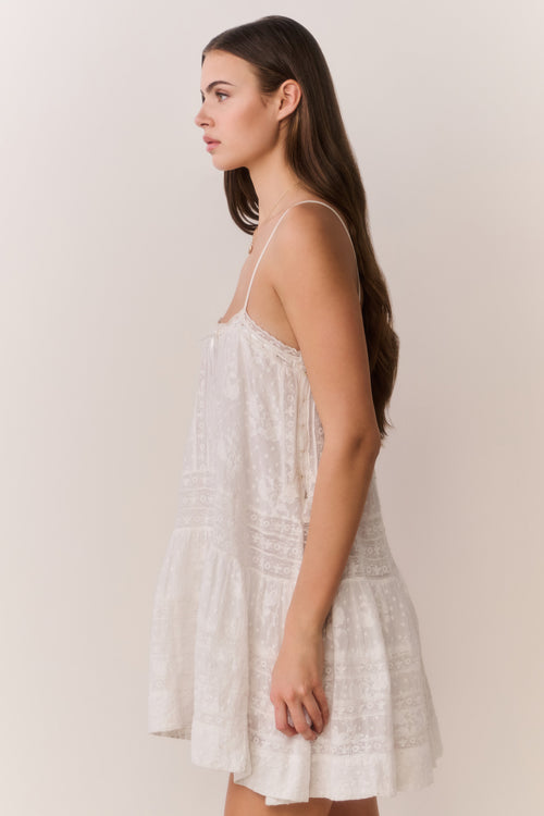 Woman wearing a white lace mini dress against a plain background